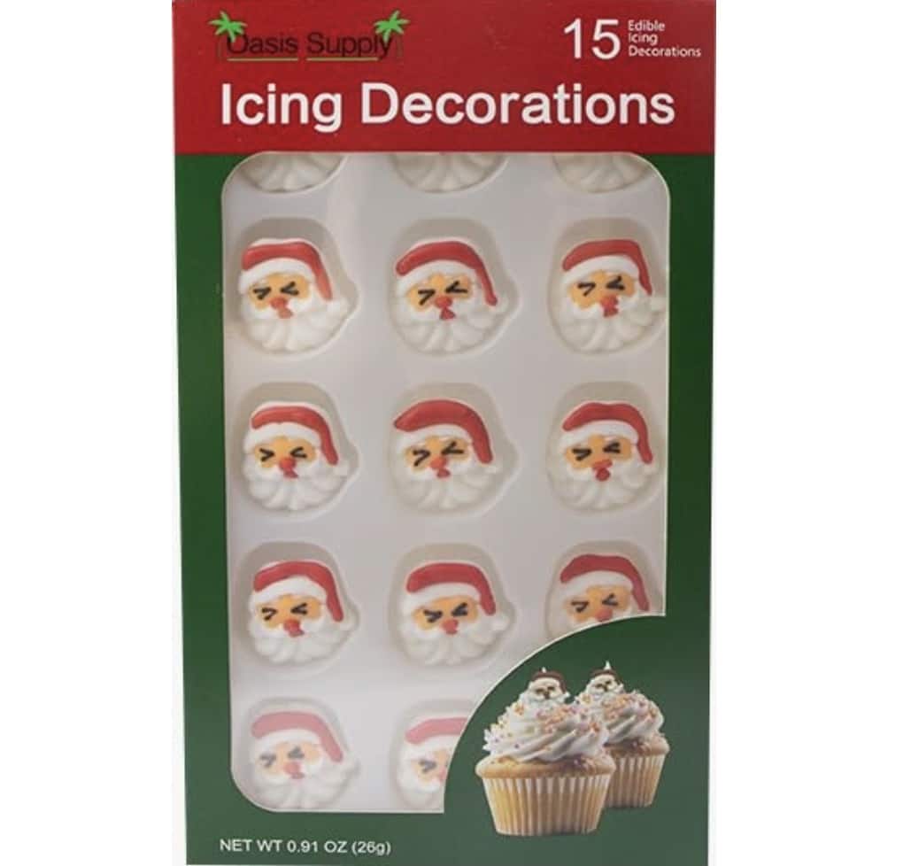 A pack of 15 edible icing decorations featuring Santa Claus faces, perfect for topping Snow Globe Cookies, packaged in a green and red cardboard box. The front displays several Santa designs and an image of cupcakes with the icing on top.